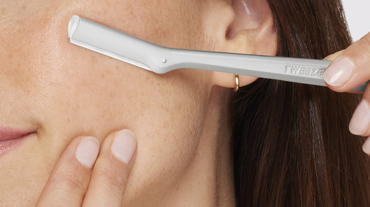 Person using a FACIAL RAZOR on their face with a close-up view.