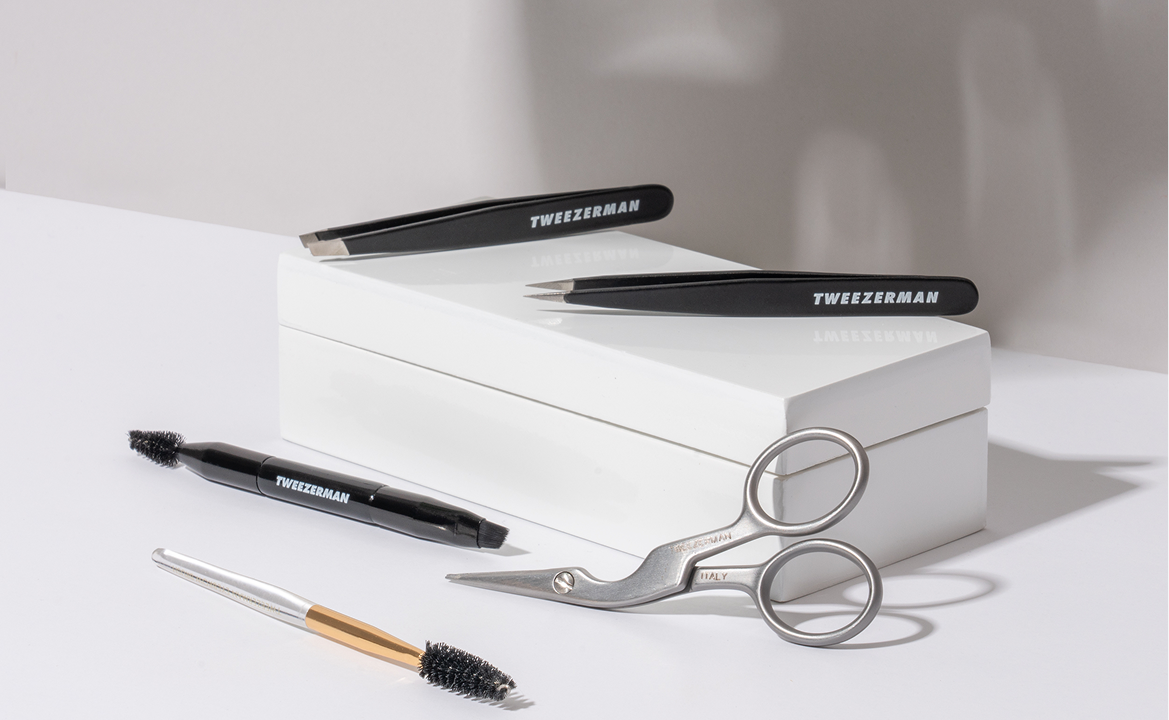 Assortment of Tweezerman Beauty Tools laid out on a clean white counter with white box.