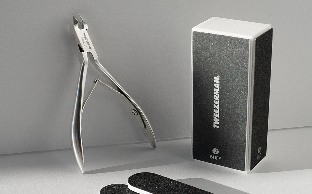 Tweezerman Stainless Steel Rockhard Cuticle Nipper, Black Nail Files  and Nail Buffer Block displayed on white counter along a white wall.