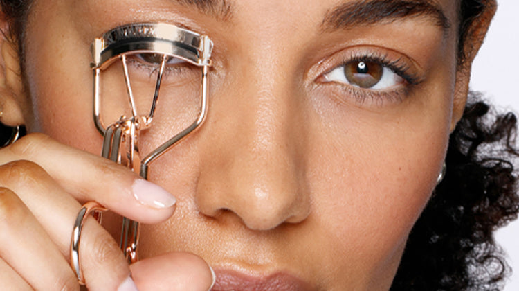 Person using an eyelash curler with a close-up focus on the eye area.