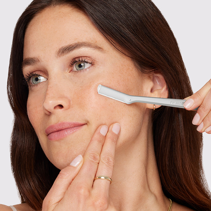 Woman using a skincare tool on her face with a plain background