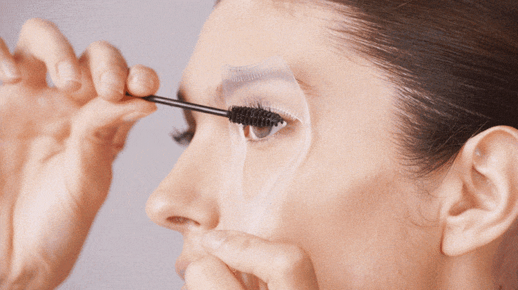 model using lash guard and comb, applying mascara with one hand and holding lash guard up to eye with other hand