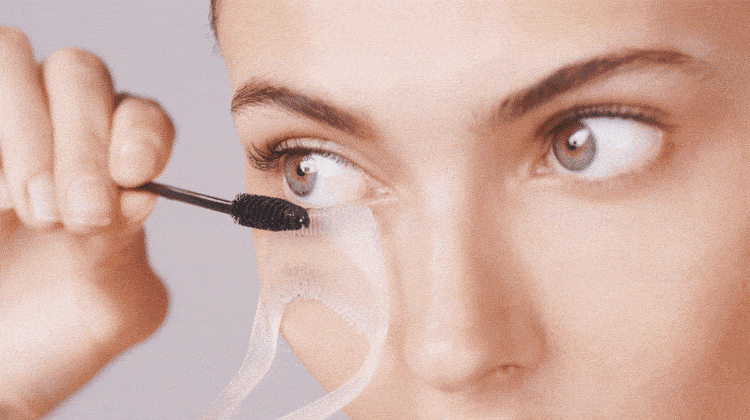 model using lash guard and comb, applying mascara to bottom lashes with one hand and using other hand to hold lash guard